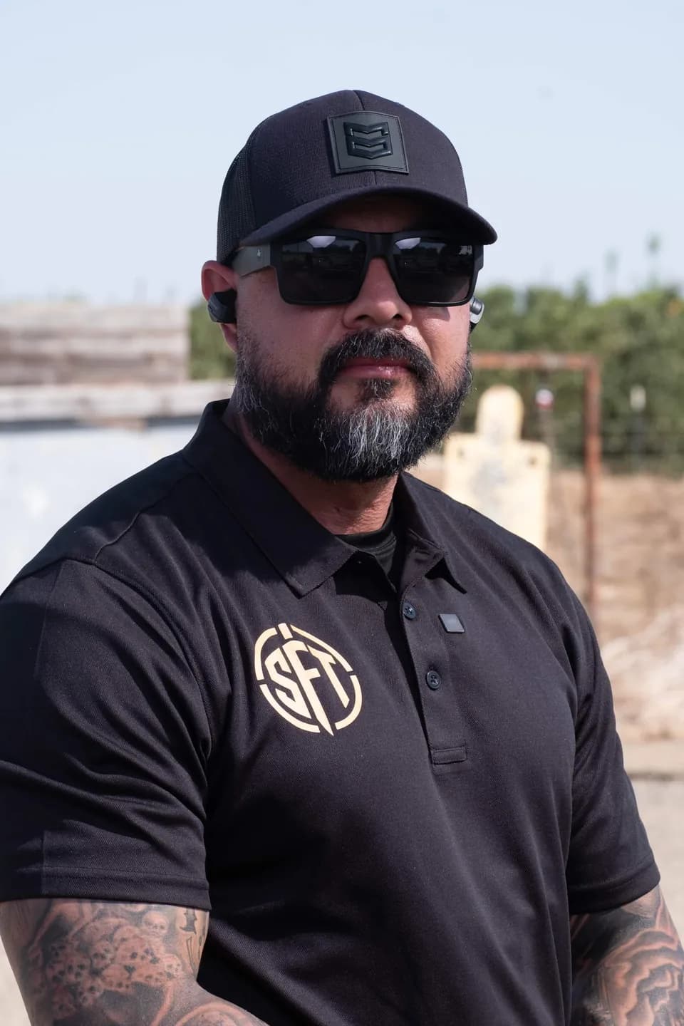 Silverline Firearms Training instructor in a black SFT polo, cap and sunglasses, standing on the range with target stands behind him.